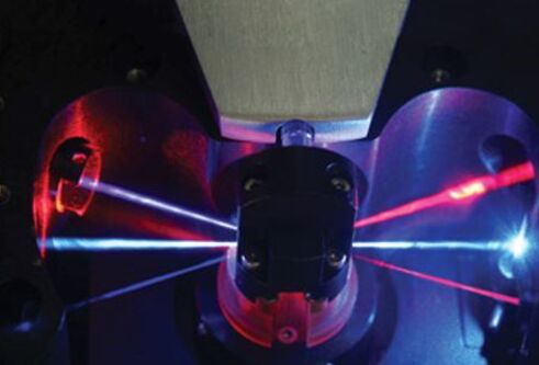 Photograph of 3 laser beams focussed through a lens, with 3 lasers of different colours leaving the lens