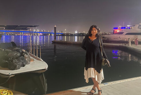 Sandra, standing at a harbour at night with yachts in the background