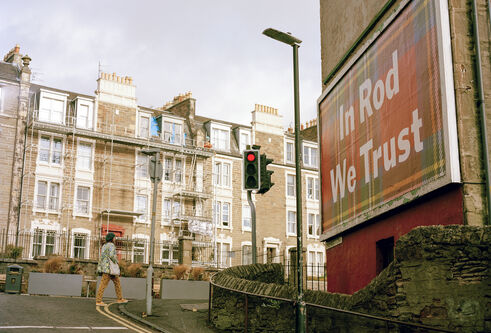A billboard with a tartan background with "In Rod we Trust" written in large white letters on a Dundee street.