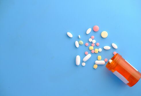 A blue background with a bottle of multicoloured pills spilled on to the surface