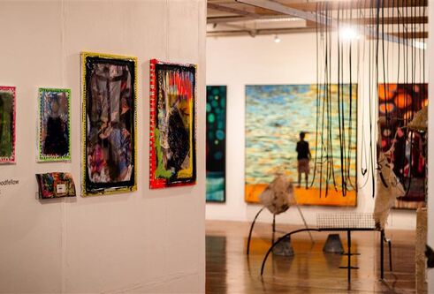 View of two walls with large artworks on them, and sculptures in the middle of a wooden floor