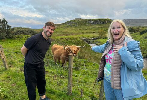 man and woman standing in front of green field with highland cow between them