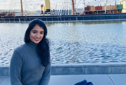 Pavithra Sundaravaradan sitting outside the V&A museum with the Discovery ship in the background