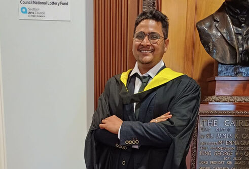 Supratim Das Gupta standing inside Caird Hall in his graduation gown