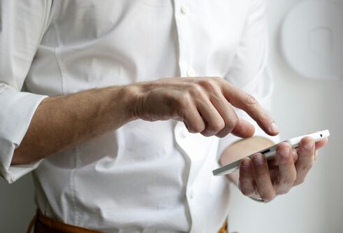 A man in a white shirt, whose face cannot be seen, using a white mobile phone