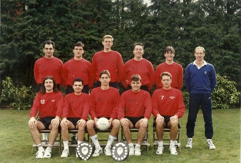 Paul McPate stand at the far right, top row with the University football team and their trophies