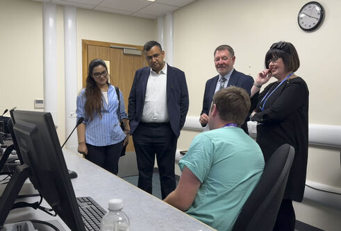 Dr Vikas Swarankar standing in room beside three people listening to a seated person in scrubs.