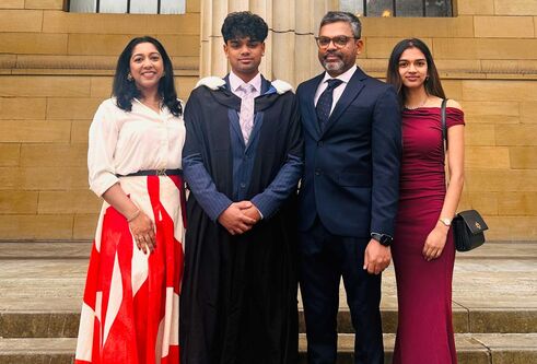 A students on graduation day posing with his family, smiling and all standing on steps outside a building, all dressed in smart wear.