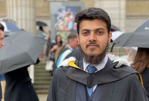 A graduate standing outside of Caird Hall in graduation regalia