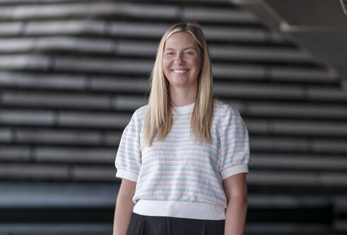 woman wearing woollen tshirt, with long blond hair, looking and smiling at camera