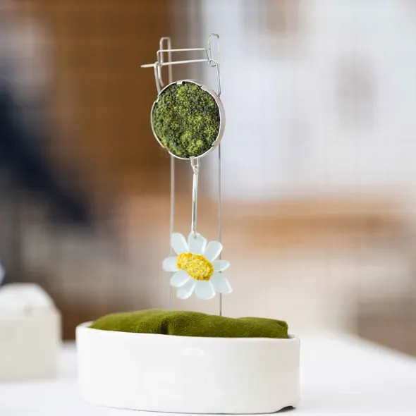 A piece of jewellery with green moss at the top and a daisy hanging below as part of the Degree Show 2025 exhibition