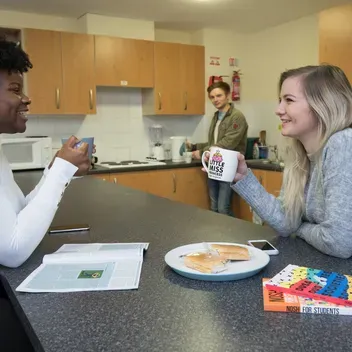 Students eating and drinking around kitchen table