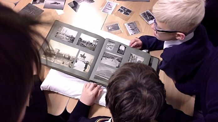 School pupils look over some archived photographs in a scrapbook