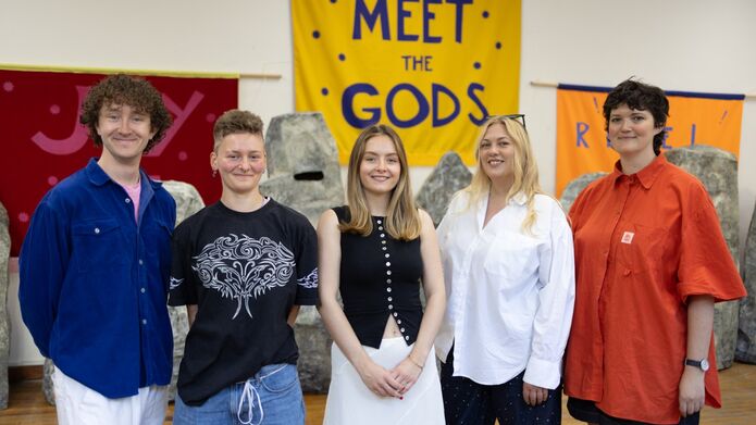 group of people standing in front of Meet the Gods sign	