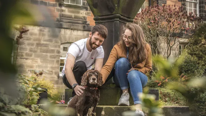 Young man and woman with brown fluffy dog in the Geddes Quadrangle