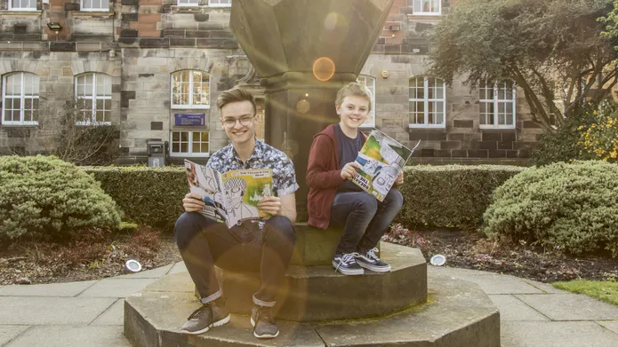 Drew Marr sitting in the University's quad holding a comic