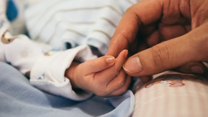 An adult holding a baby's hand