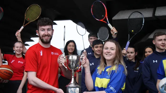 a young man in his 20's, holding half of a large silver trophy while a young woman of similar age holds the other half