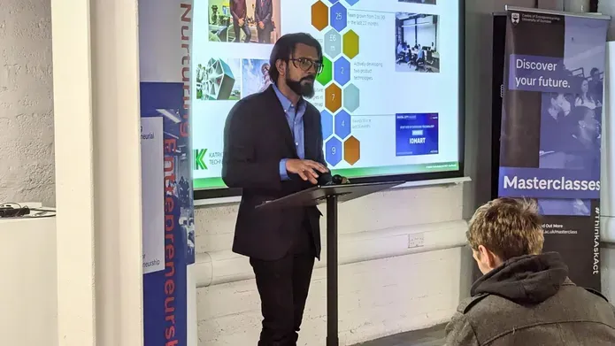 Karthik presenting at a conference standing in front of a mic with a presentation slide