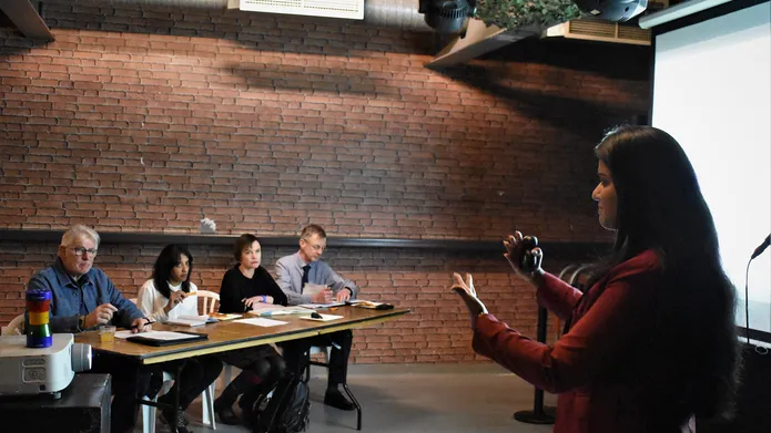 A speaker standing in front of a panel of four judges giving a talk