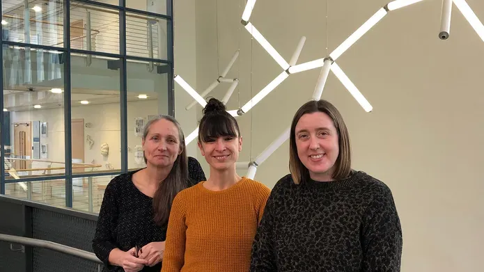 Kate, Aida, Gail standing at a balcony in Life Sciences with a DNA light fixture behind them