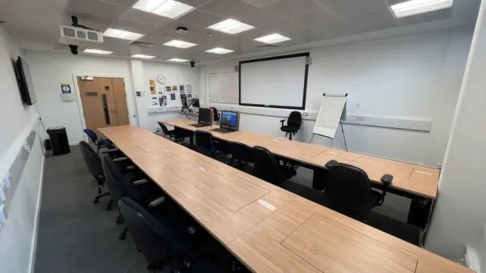 Dalhosuie 1LG02 showing two rows of desks and chairs. PCs are set inside the tables. with a white screen on the wall