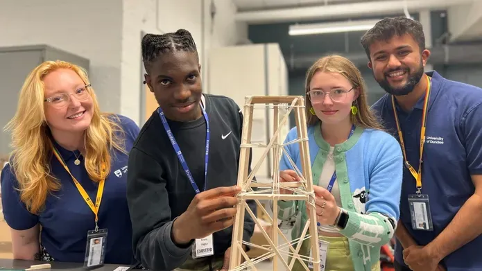 Two Dundee students and two secondary school pupils pose around a mock-up rocket landing tower build, made out of wood