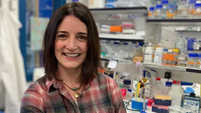 Leeanne McGurk in a lab with rows of bottles on shelves behind