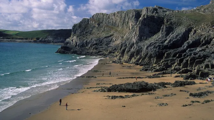A coastline with a big sandy beach, ocean and rocky cliffs.