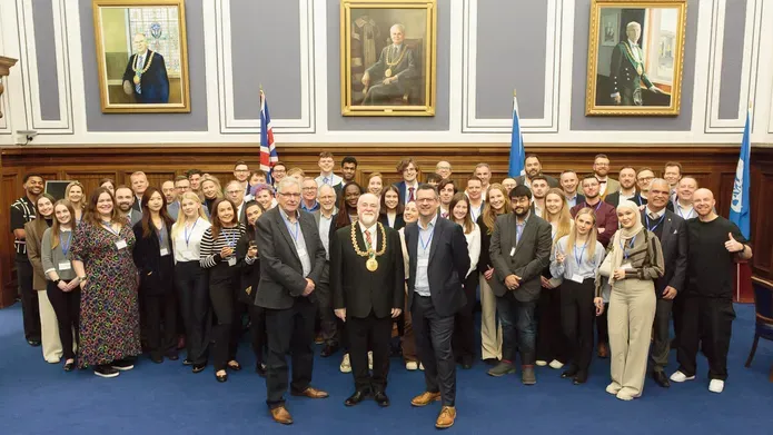 A large group of people dressed smartly stand in front of three large portraits.