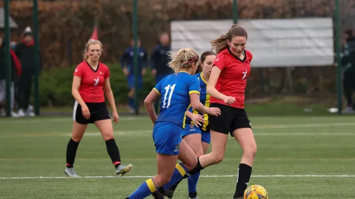 action shot of women playing football. Player with red has ball and player with blue is going in to tackle