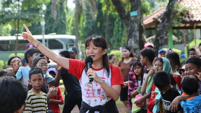 Lina speaking into a microphone surrounded by children