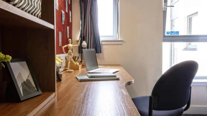 A close up of a study area in a student room with a laptop on the desk and shelving