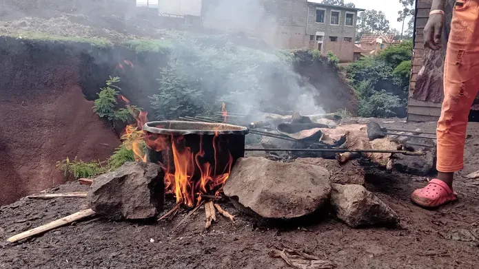 Open fire with cooking pot, and person standing nearby in orange trousers