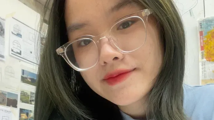A person with shoulder length straight brunette hair and glasses, wearing a blue jumper.