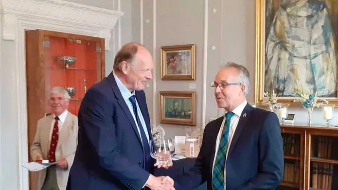 Two men wearing suits shake hands.