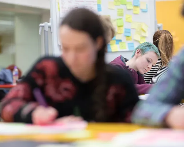 students working with sheets of paper covered in post-it notes, more post-its are on the wall behind