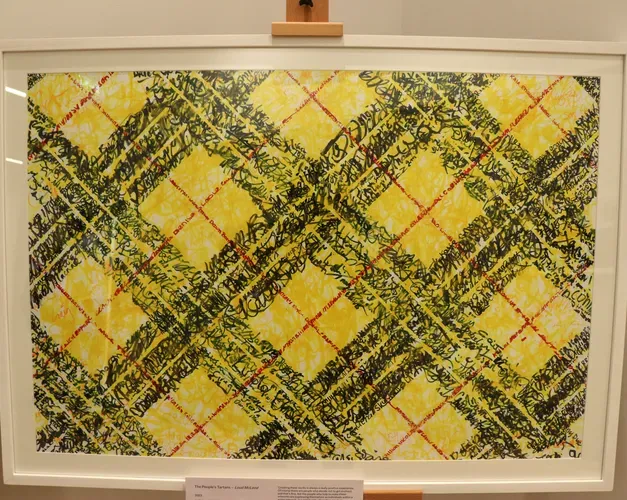 An image of yellow black and red tartan in a white frame on an easel