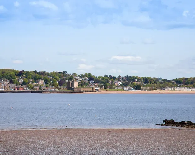 Sandy beach looking out towards sea, over to another sandy beach and town built onto a hill.