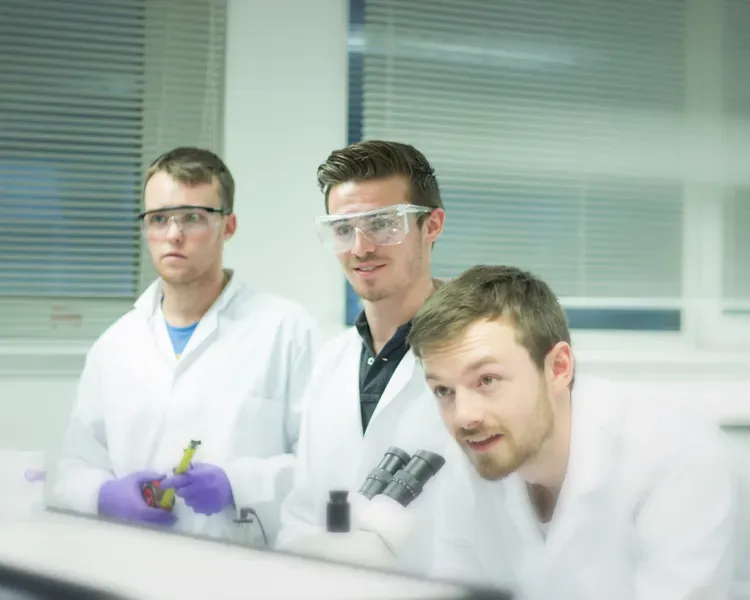 Three students using a microscope in a lab