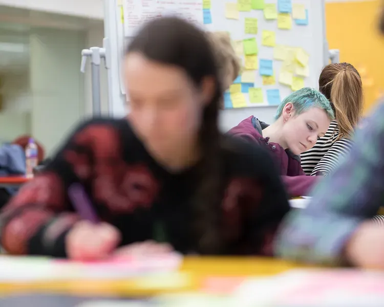 students working with sheets of paper covered in post-it notes, more post-its are on the wall behind