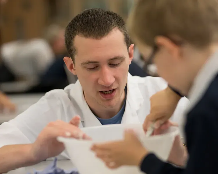 Male student showing piece of paper to primary school child