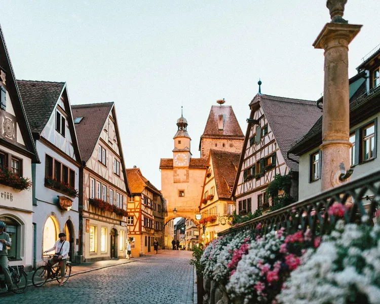 A medieval Bavarian town centre with flowers and people on bikes in Bavarian dress.