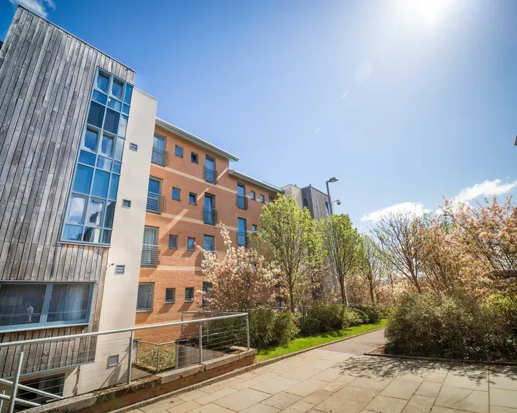 A block of timber glad flats, with a paved pathway and trees between buildings.