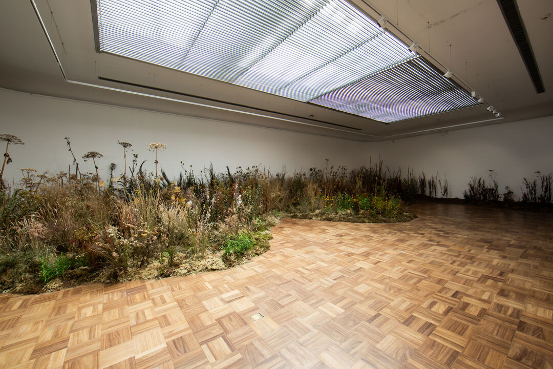 Flowers arranged like a meadow on the wooden floor of the gallery space