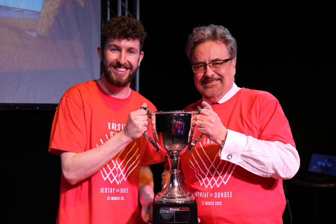 young man in his 20's standing by middle aged man, both holding one end of a large silver trophy