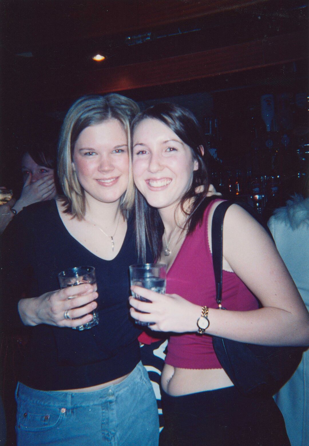 Sheryl Bartlett and friend stand together in a bar, holding a drink each.
