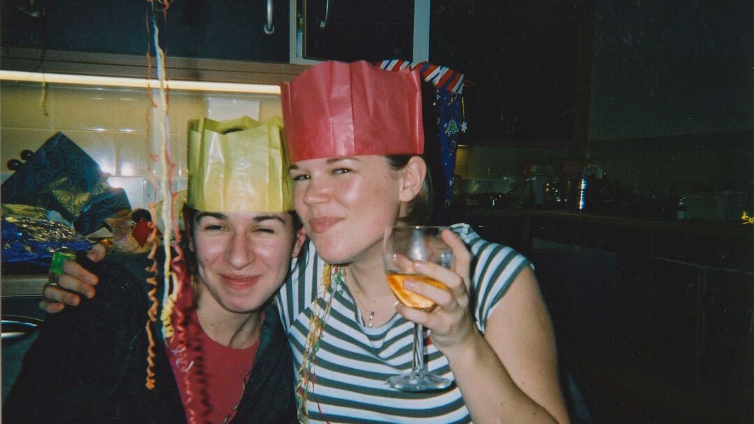 Sheryl Bartlett has arm around friend and holds glass of wine. Both girls wear Christmas party hats.