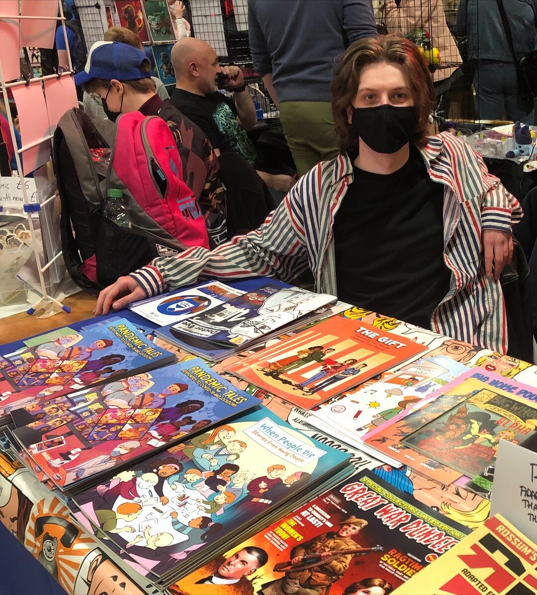 A student sits at a table covered with comics at DeeCON