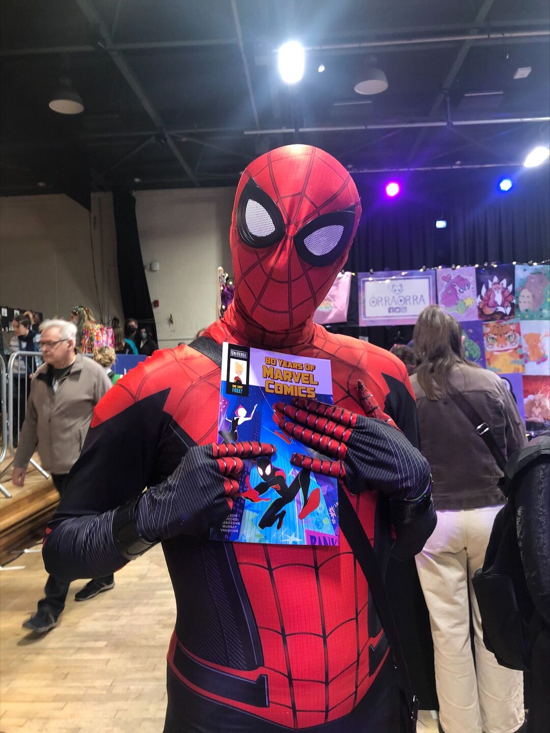 DeeCON attendant dressed as Spiderman, holds a comic against their chest.